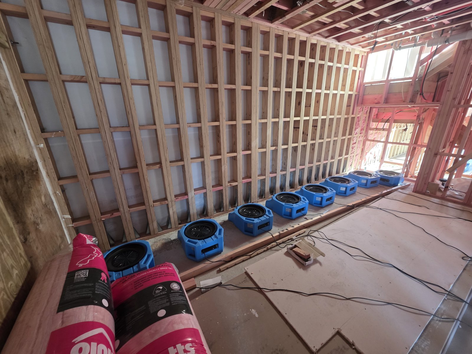 Row of ProDry air movers drying new-build wall framing with pink insulation